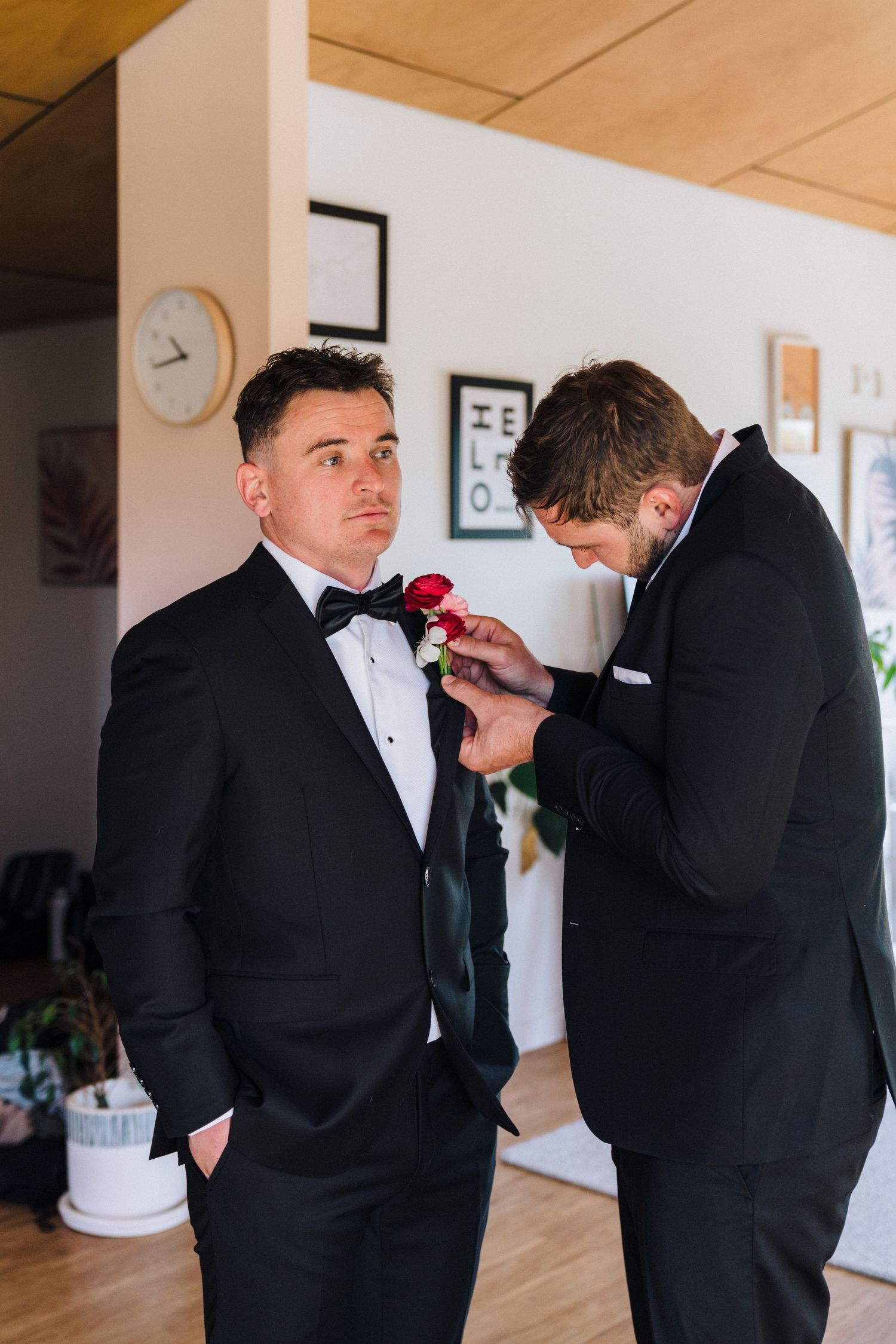 Groomsmen help each other adjust bow ties and boutonnières before a formal wedding ceremony.