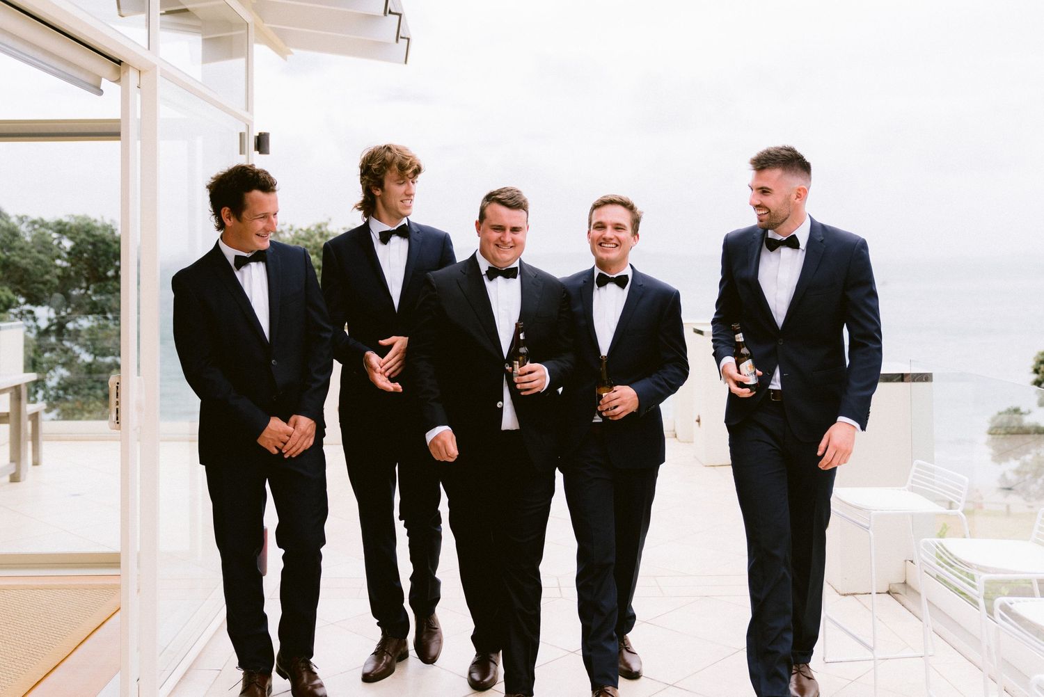 Wedding party in formal attire walks together along a white pathway.