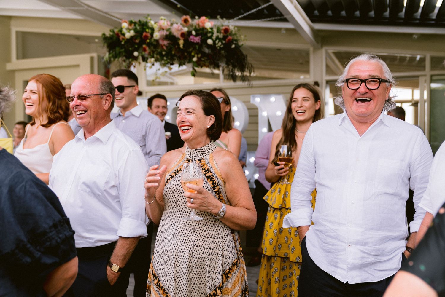 Wedding guests enjoying celebration in a bright indoor venue with floral decorations.