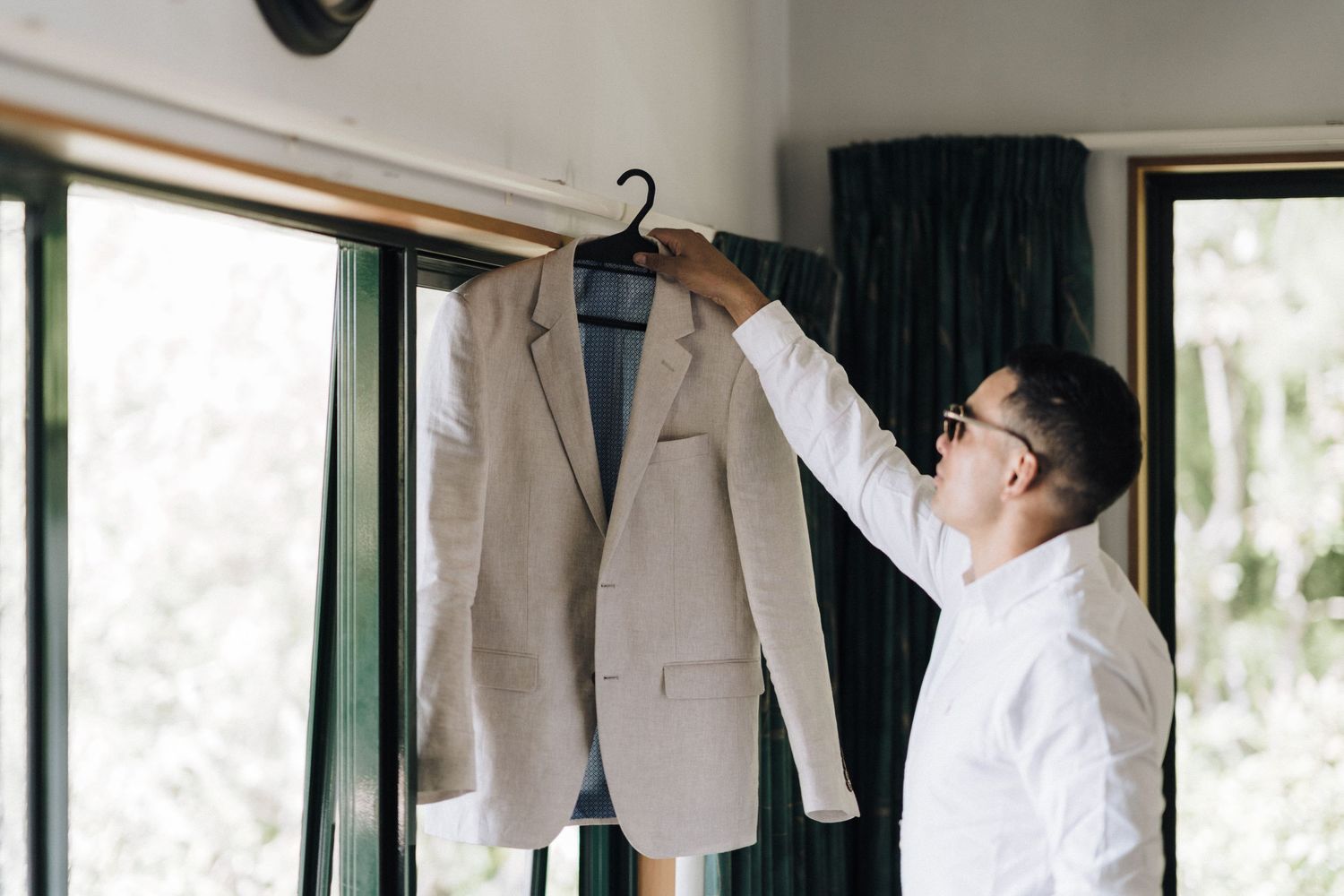 A wedding party stands lined up in a bright room with three jackets hanging on hangers behind them.