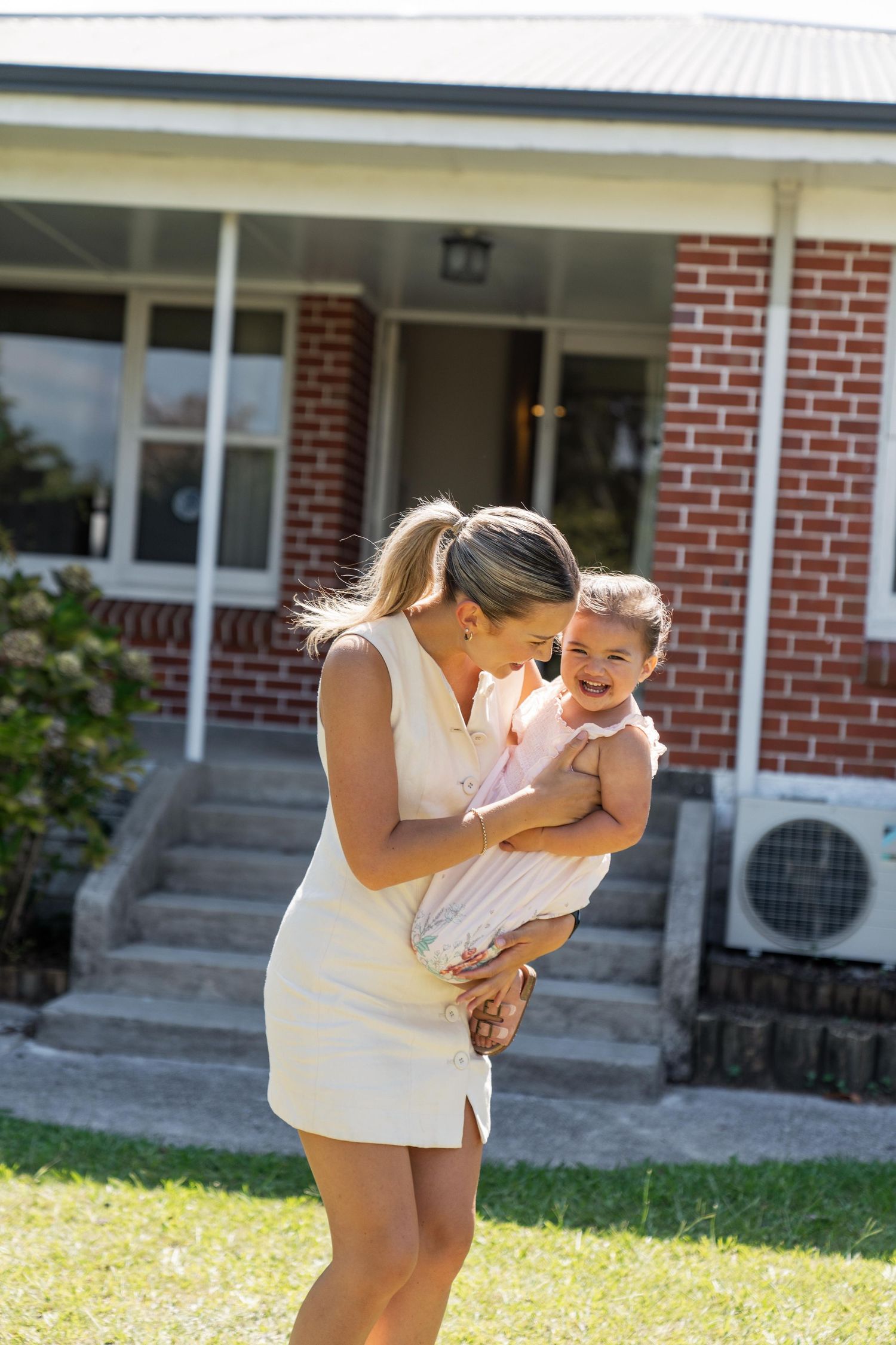 Joyful laughter shared in the sunny front yard of a brick house.
