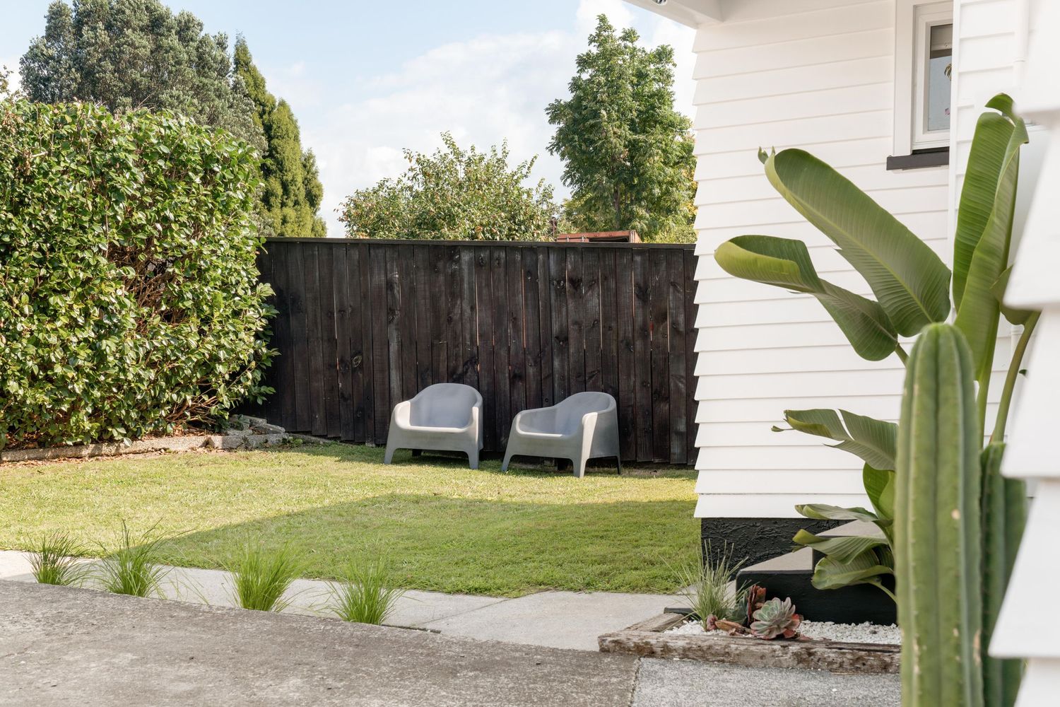 Modern backyard patio with two gray Adirondack chairs against a dark wood fence and tropical plants.