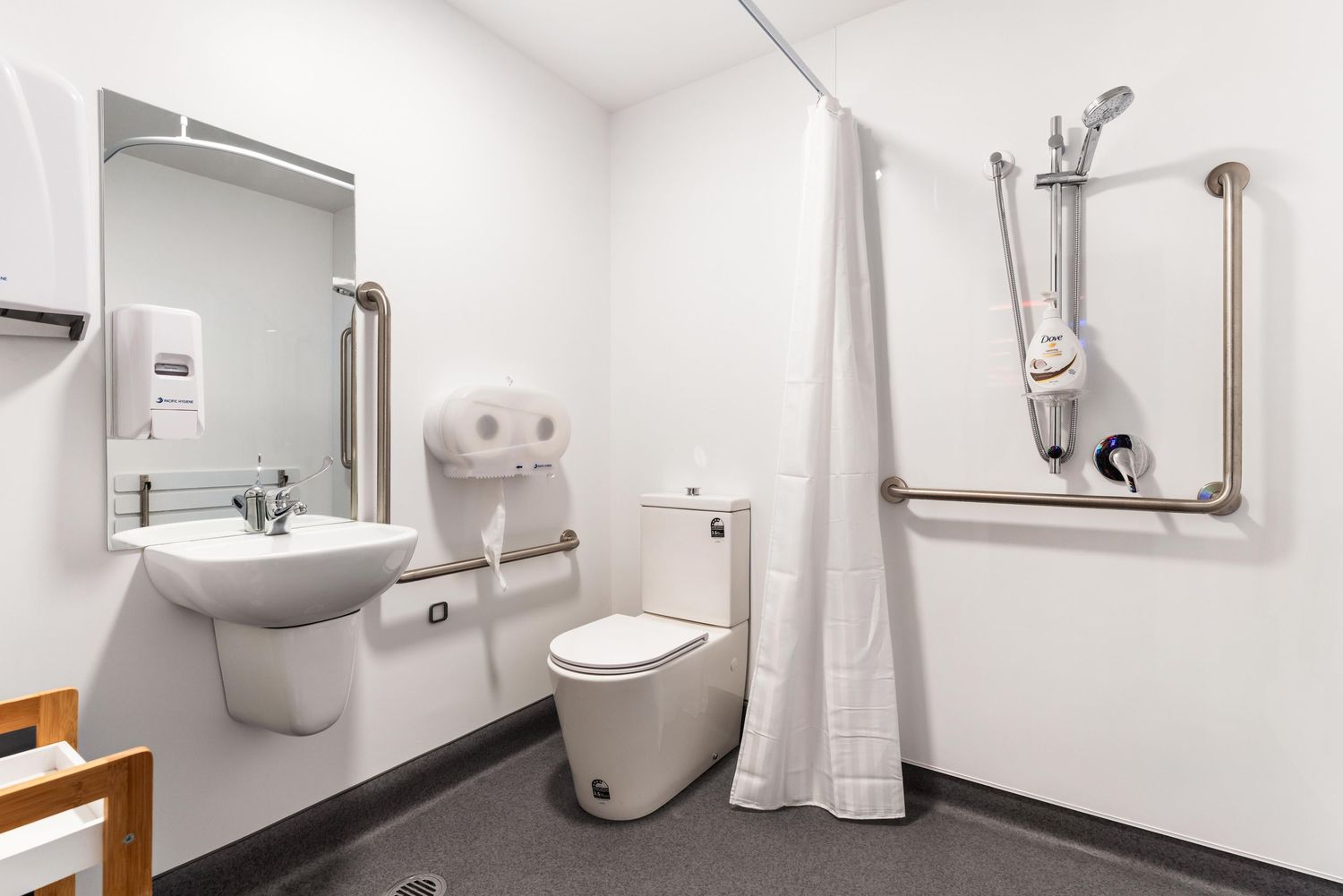 Clean modern accessible bathroom with white fixtures and safety handrails.