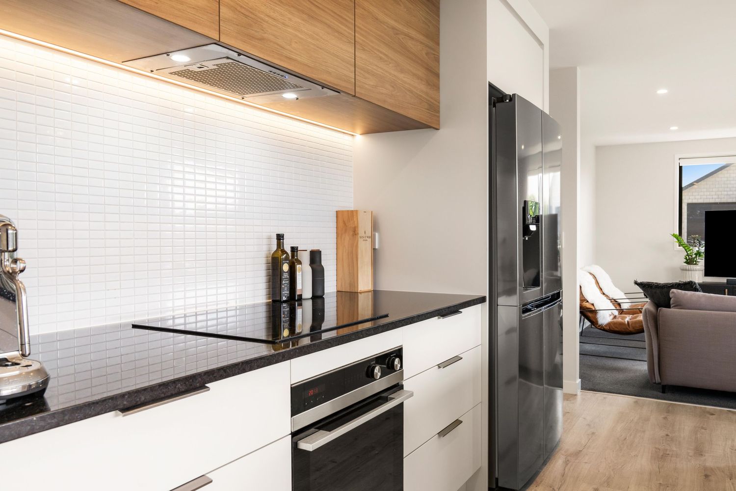 Modern kitchen with white cabinets, black countertops, wood upper cabinets, and subway tile backsplash under cabinet lighting.