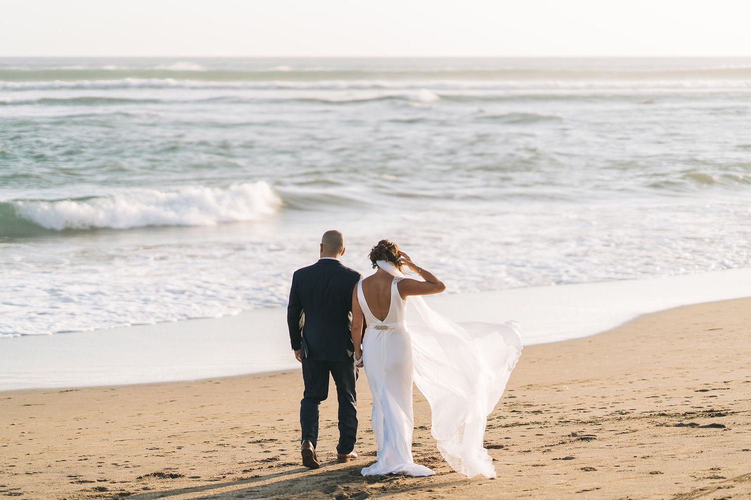 Couple walks along beach shore with waves crashing behind them.