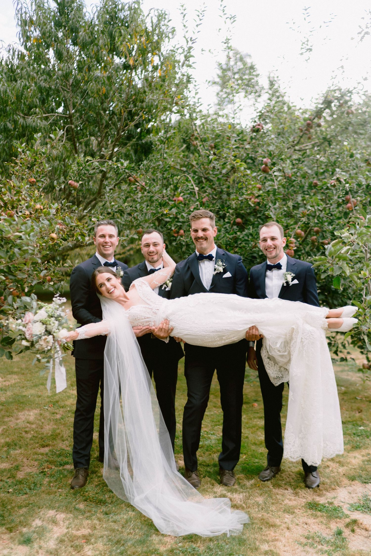 Wedding party poses playfully in a garden setting with formal attire and festive expressions.