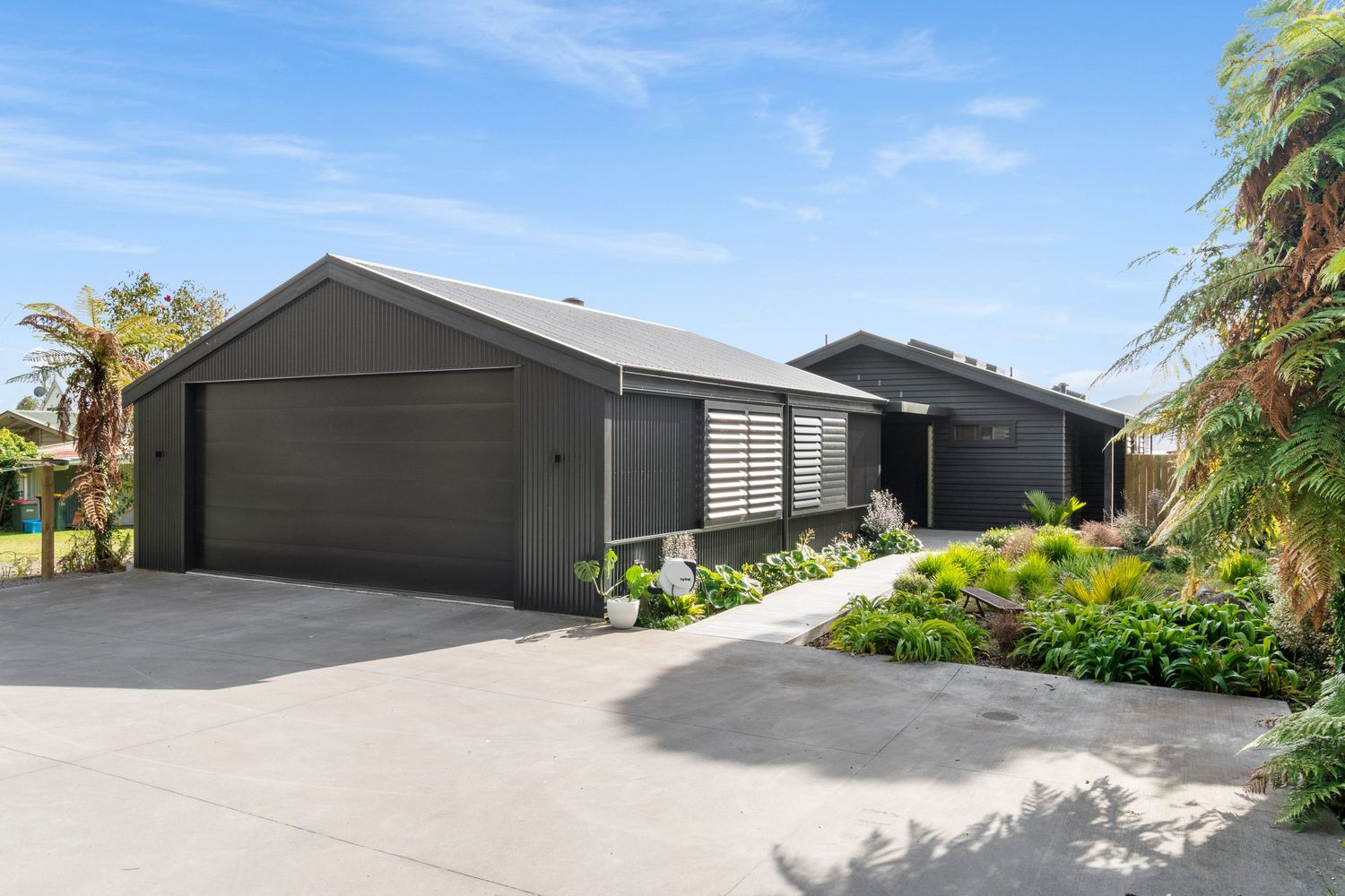 Modern single-story house with dark gray exterior, attached garage and landscaped garden on concrete driveway.