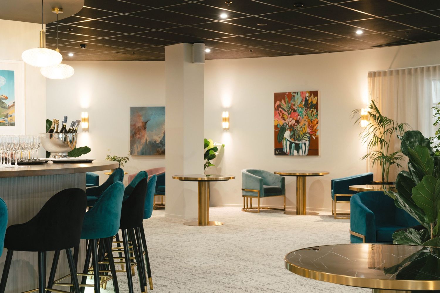 Modern restaurant interior with teal velvet chairs, round wooden tables, and stylish wall art in a bright white space.