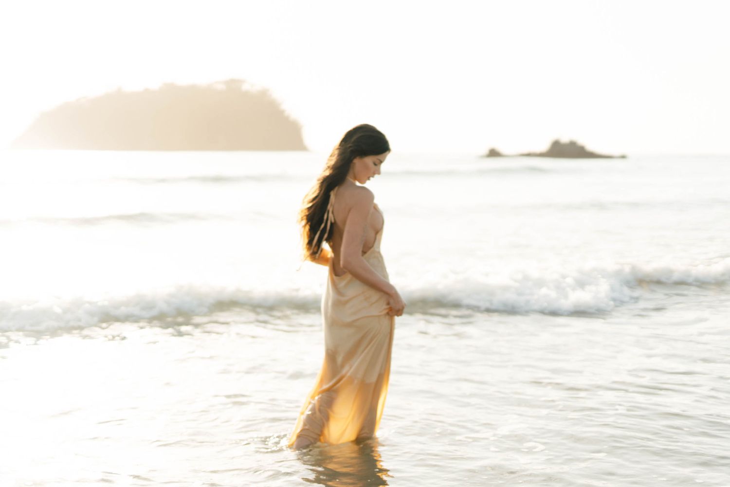 Ethereal beach scene with a person walking through waves at sunset.