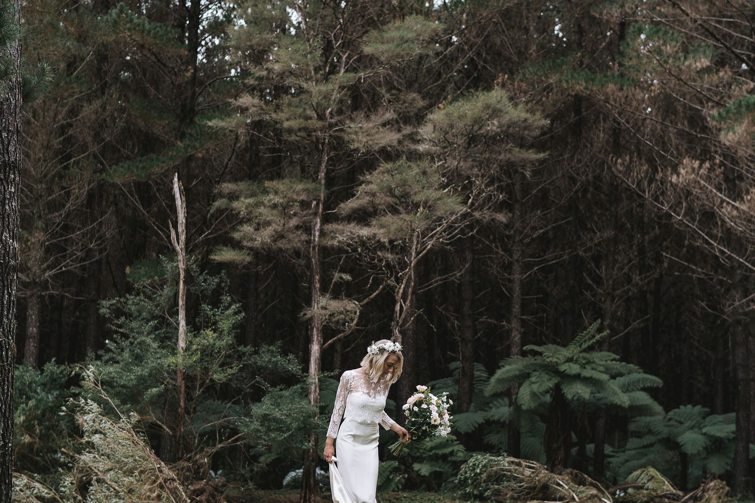 A person in a white dress stands among tall ferns and trees in a mystical forest setting.