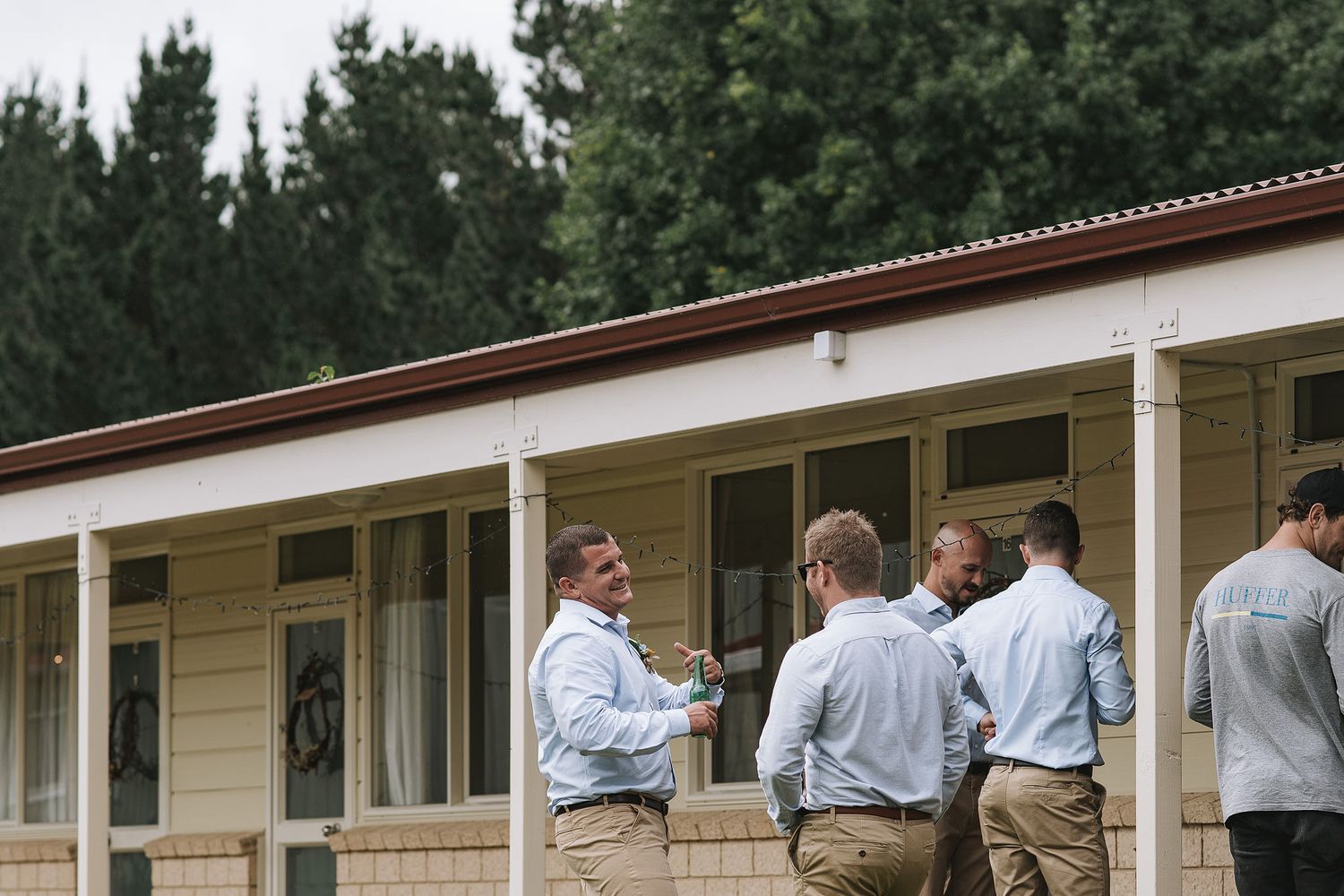 A group of people in casual business attire gather outside a long white building with covered porch columns.