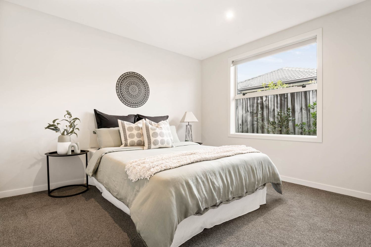 Contemporary bedroom with gray carpet, white walls, and circular wall art above the bed.