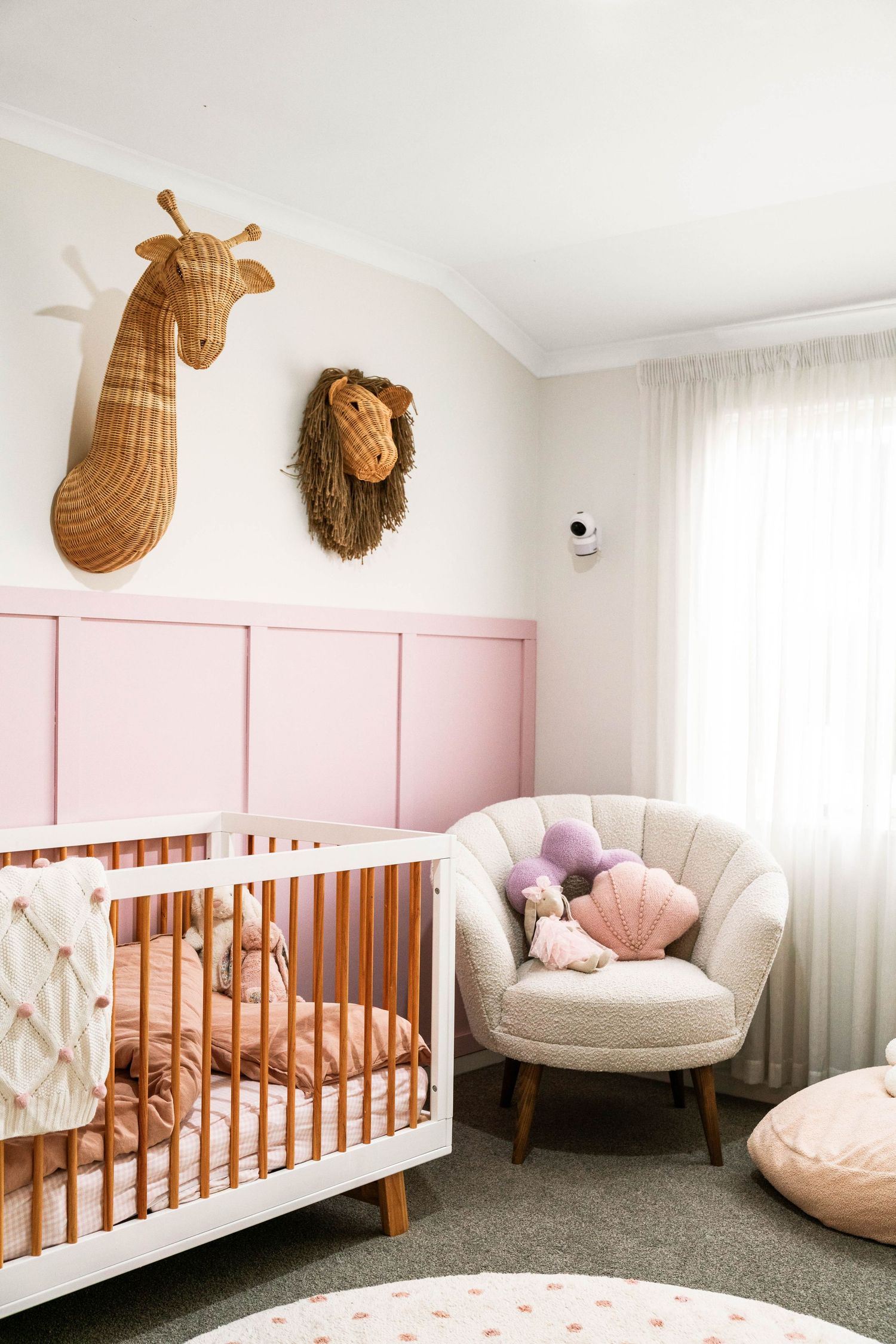 Nursery with pink wainscoting, wooden crib, plush chair and woven animal wall decor.
