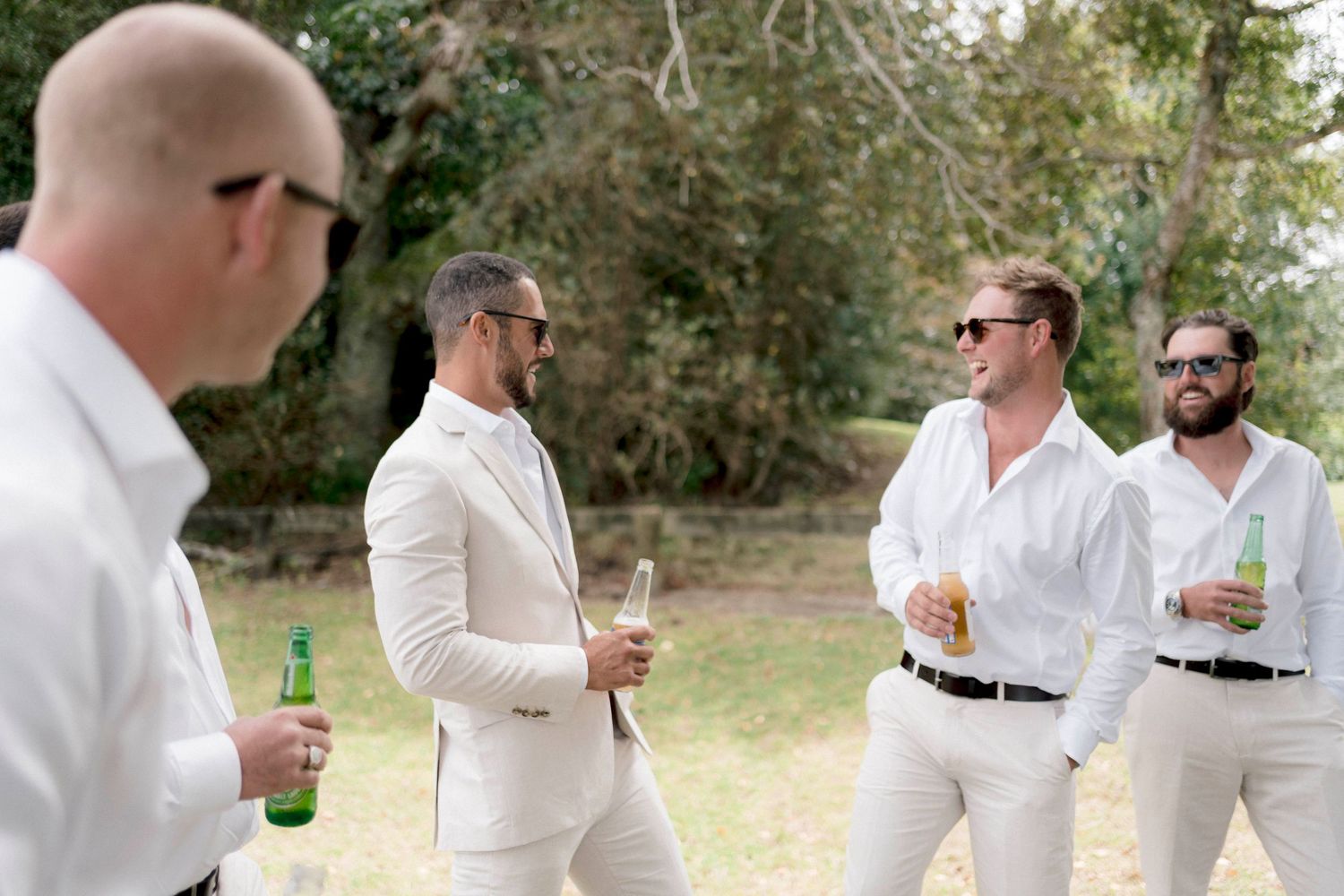A group of people wearing white outfits gather outdoors holding drinks and engaged in conversation at a social event.