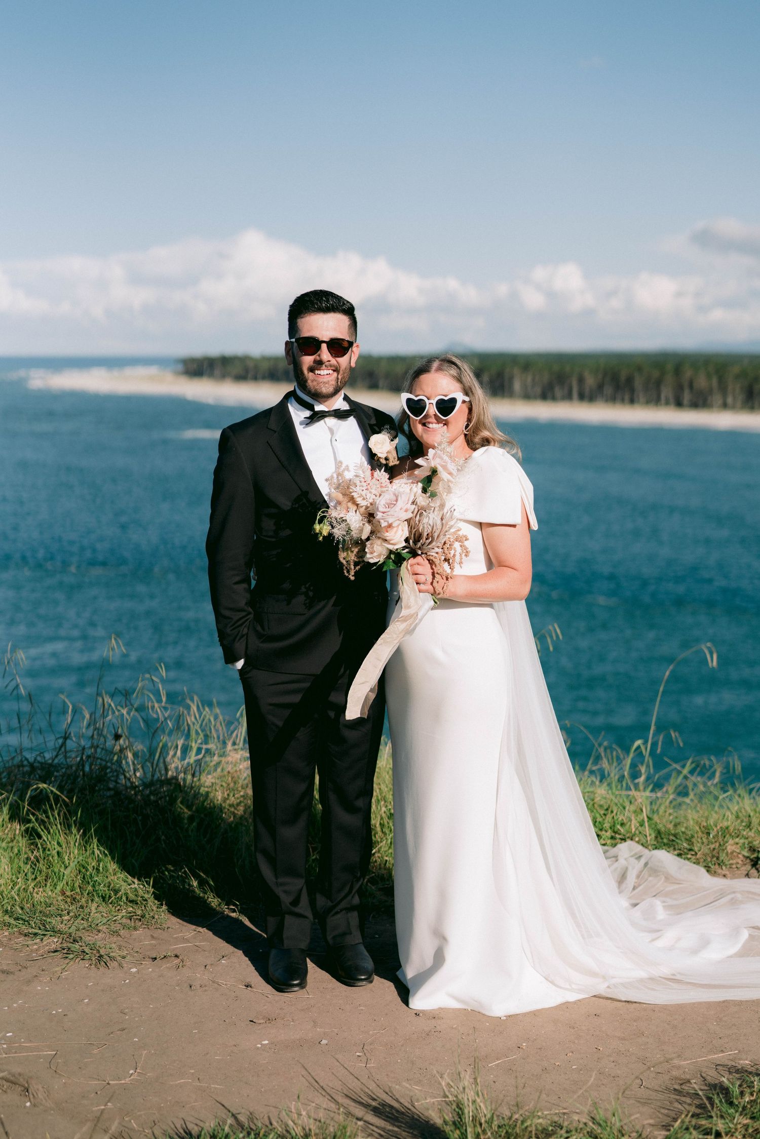 Newlyweds pose for romantic coastal photos with ocean and cliffs as backdrop.