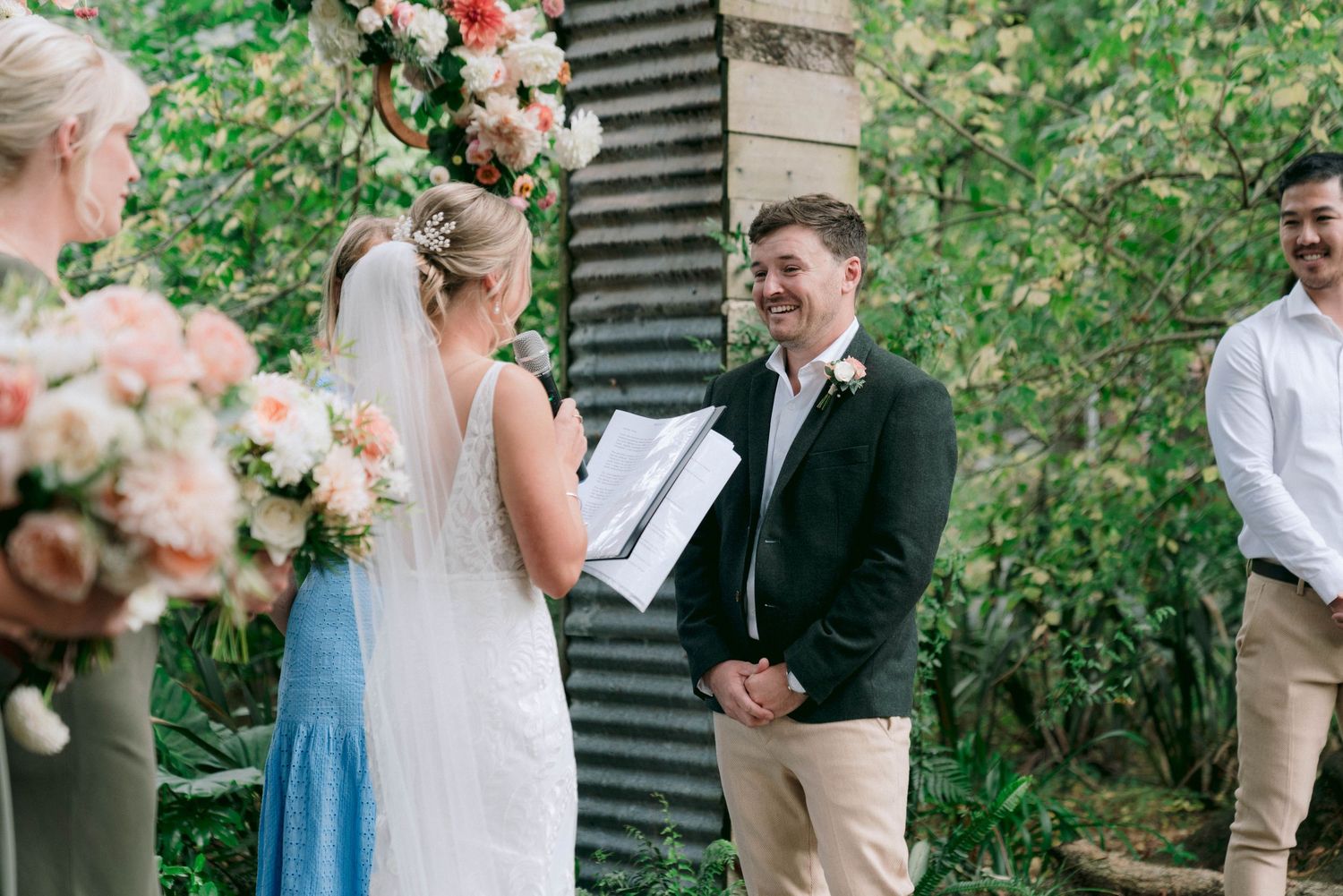 Wedding ceremony in progress under floral arch with blue bridesmaid dress visible.