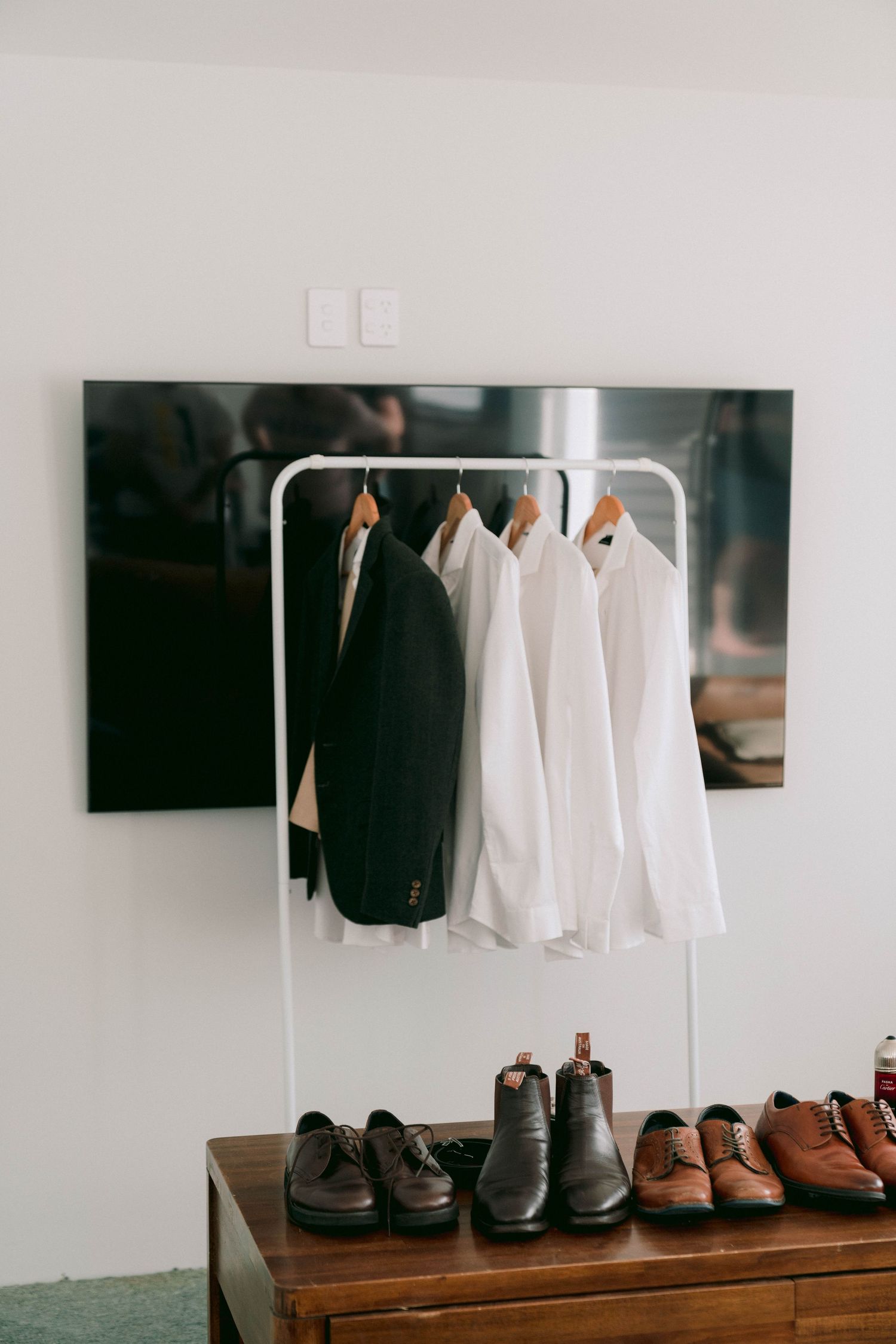 White dress shirts and dark suits hanging on minimalist clothing racks with brown dress shoes lined up below.