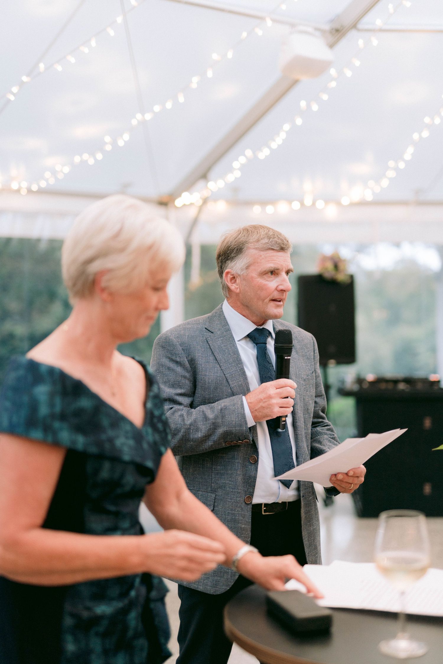 Wedding reception speech under a tent decorated with string lights.