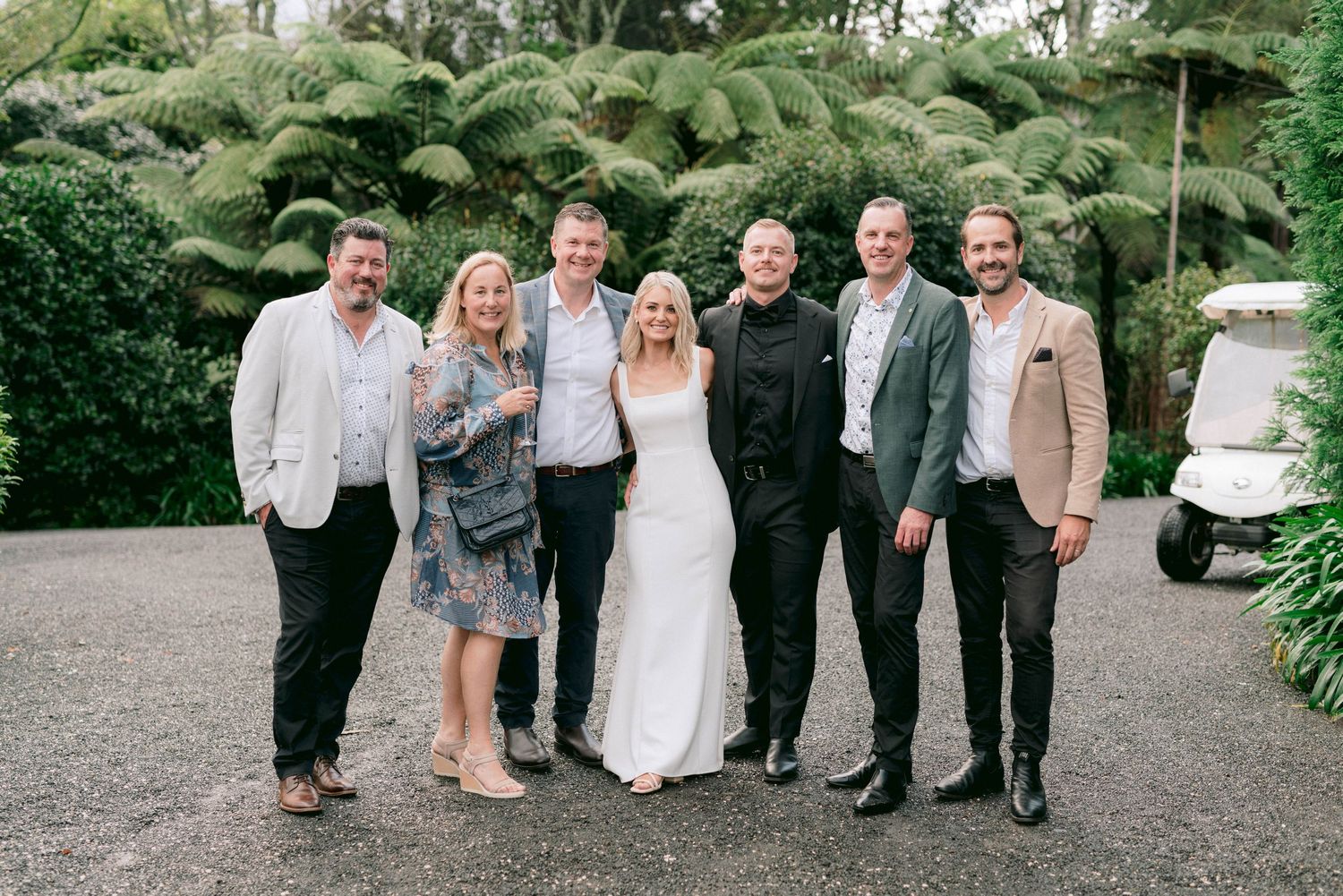 Wedding group photo with the newlyweds and guests on a garden path surrounded by greenery.
