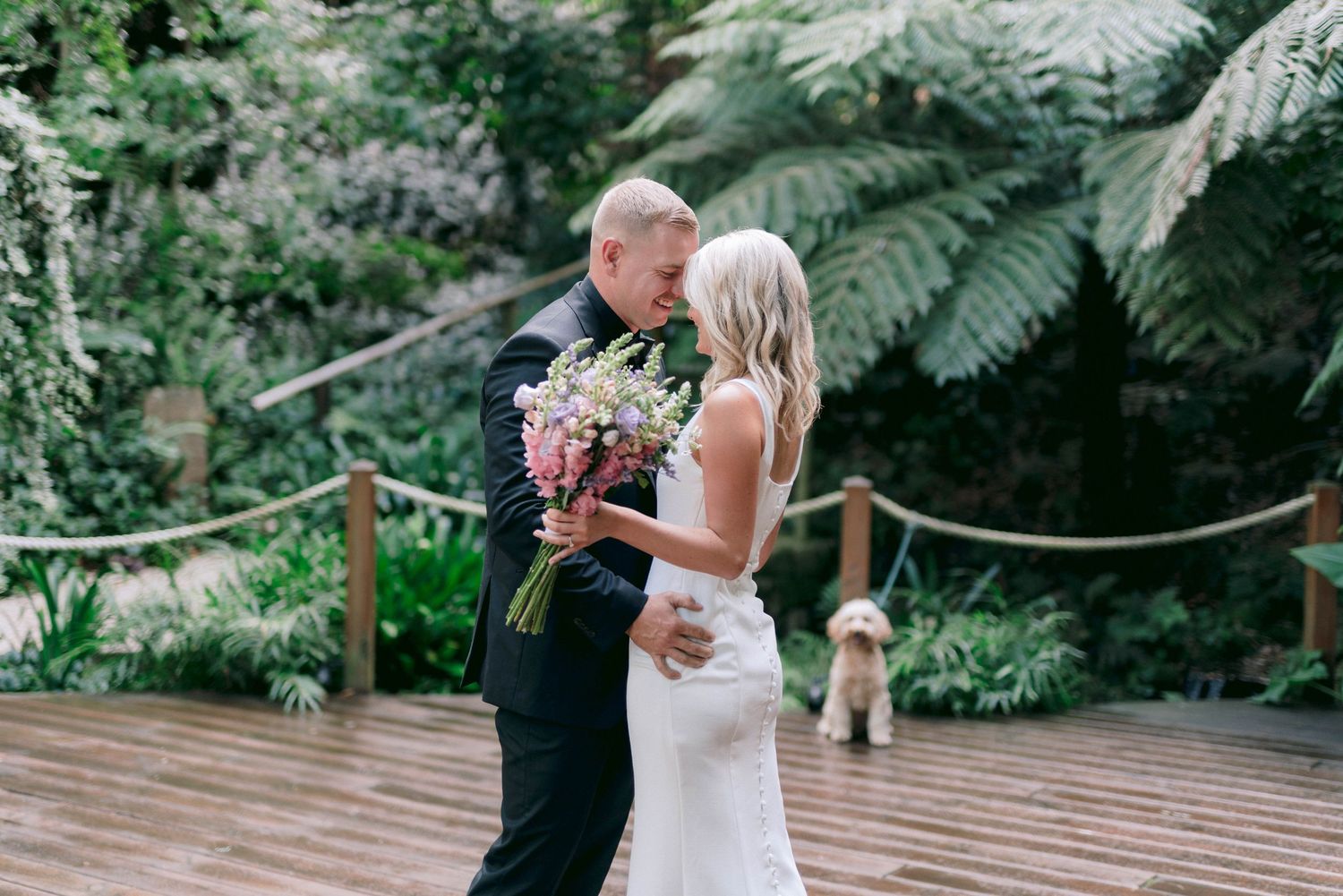 Two people share a romantic dance moment on a wooden deck surrounded by lush tropical greenery and ferns.