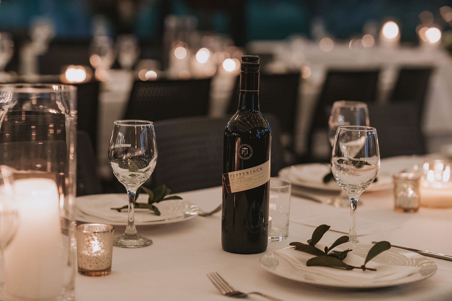 Elegant table setting at upscale restaurant with wine bottle, wine glasses, and candlelight creating romantic ambiance.