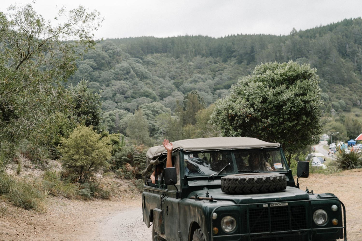 A vintage Land Rover Defender parked on a dirt trail in a mountainous forest landscape.