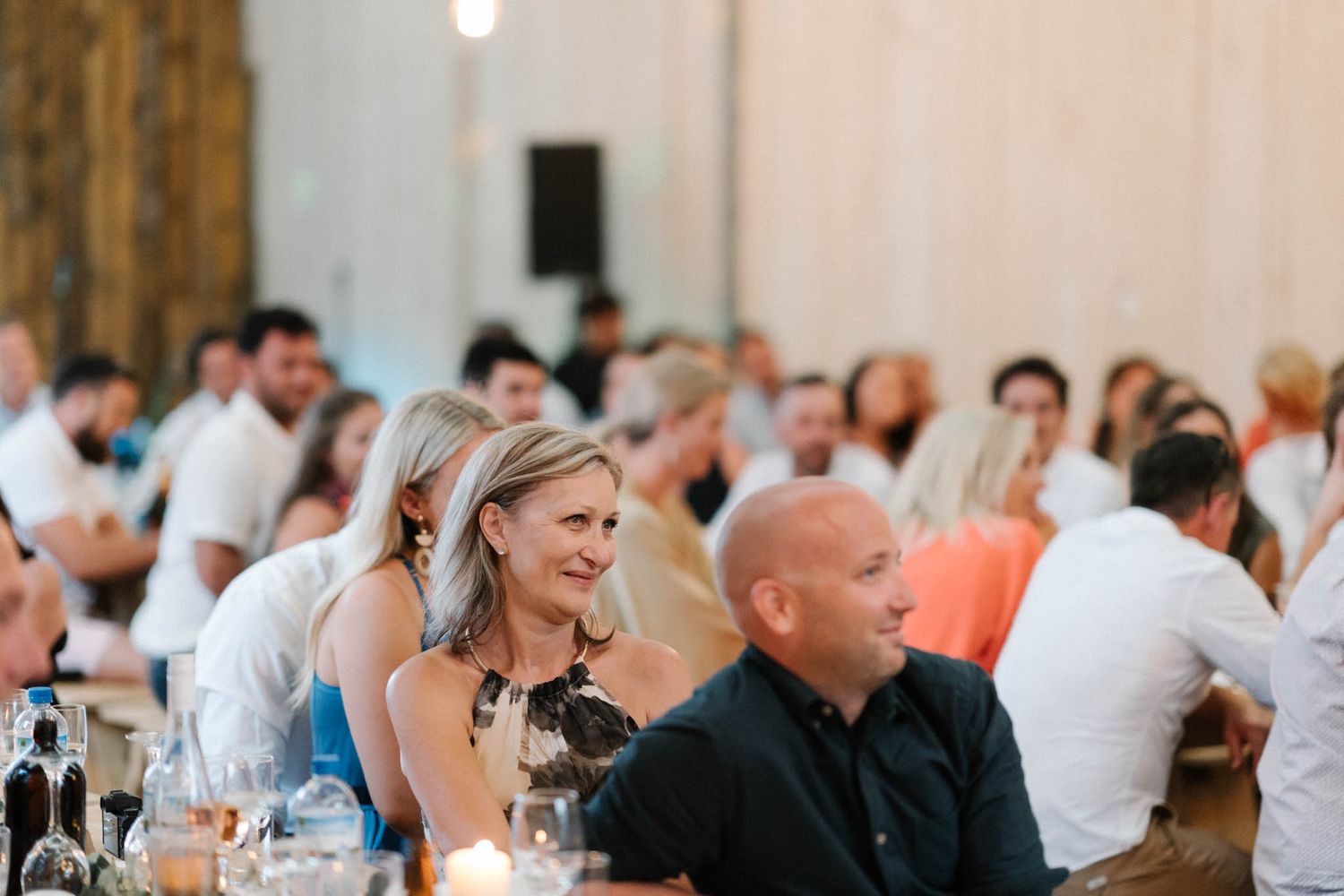 Wedding guests enjoy a lighthearted moment during the dinner reception in a rustic venue with wooden details.