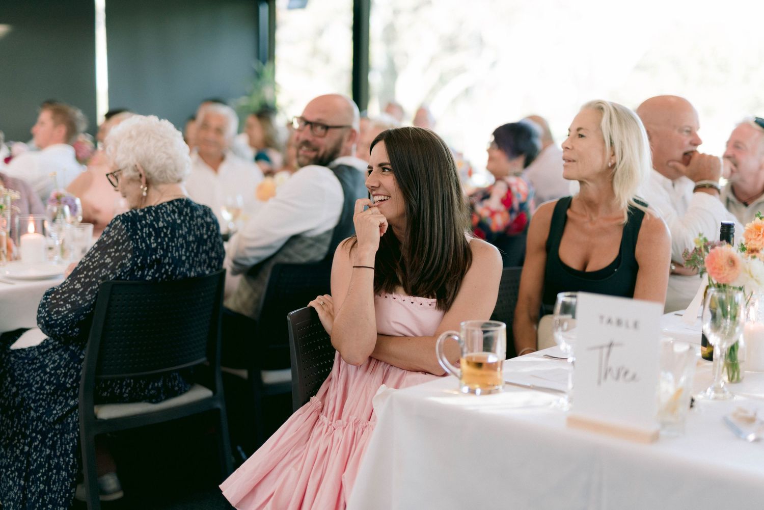 Wedding reception guests seated at tables with pink decor enjoy the celebration.