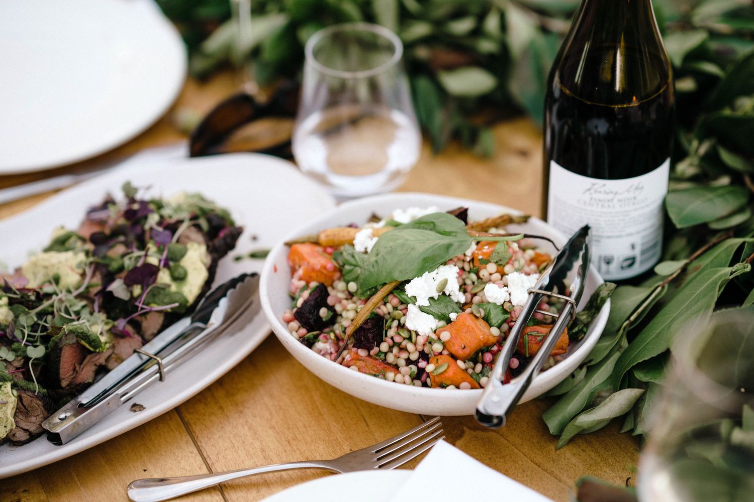 Elegant table settings with wine bottles, greenery and rustic decor at an outdoor wedding reception.