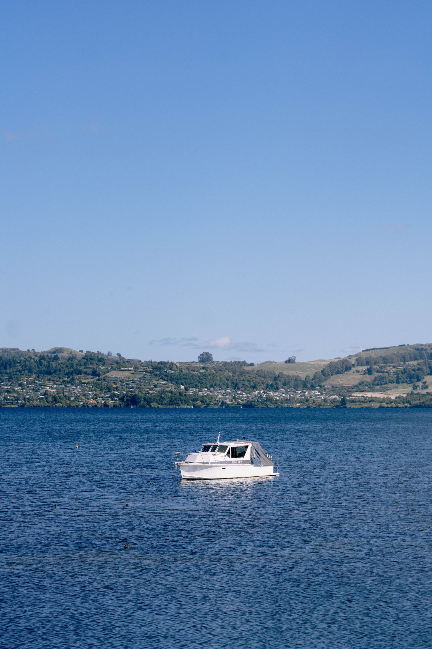 A white motorboat cruises across calm blue waters with rolling hills and mountains visible along the distant shoreline.