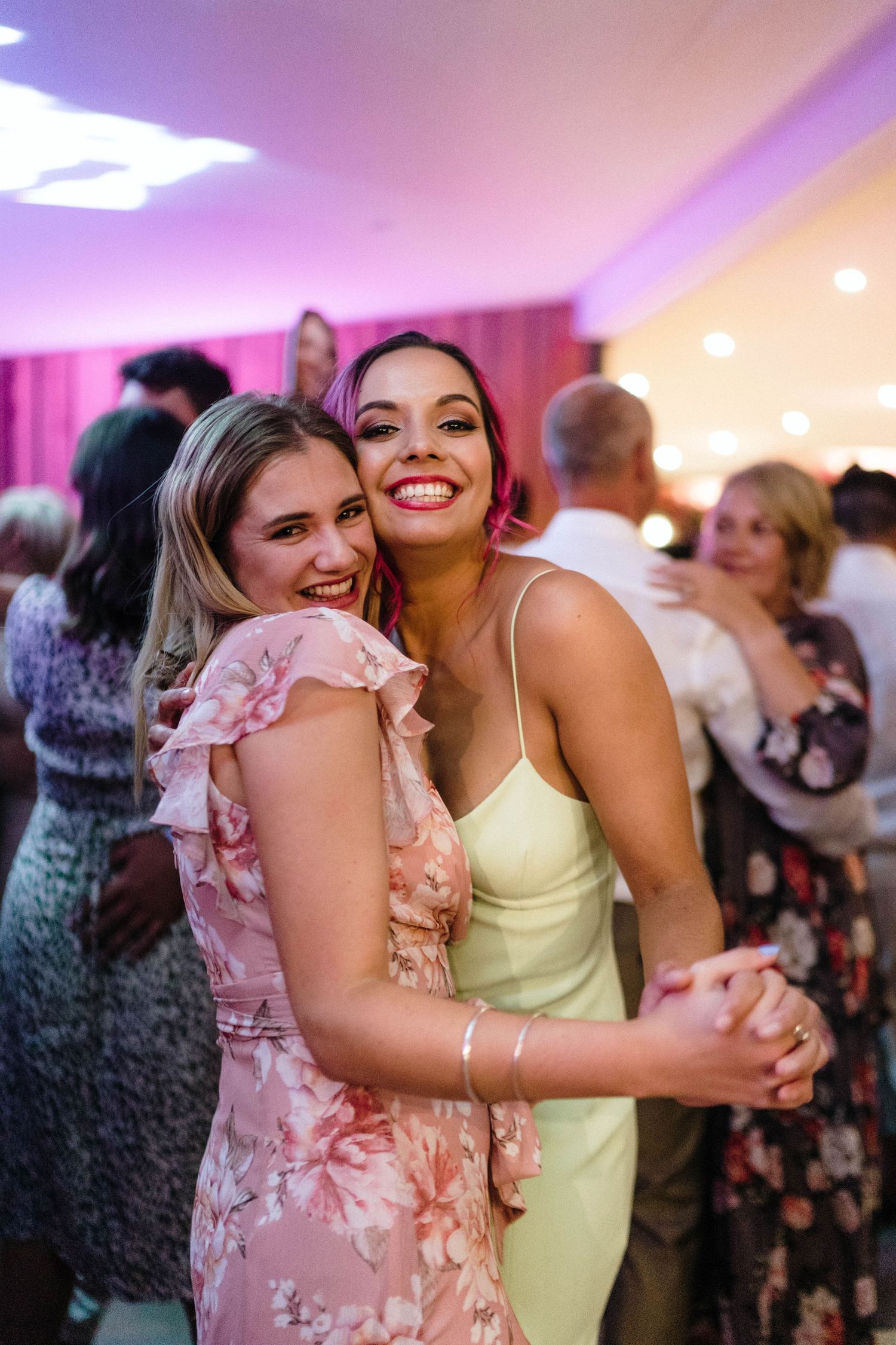 Two guests dancing together at wedding reception with pink lighting.