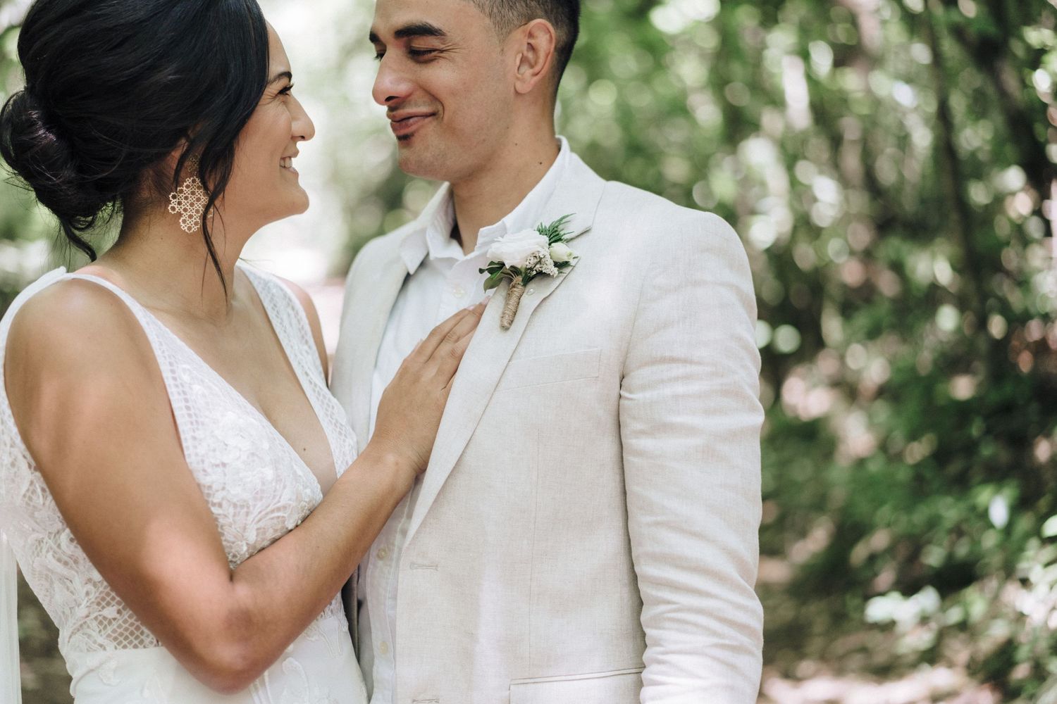 Elegant couple in white attire share intimate moment during outdoor garden photoshoot.