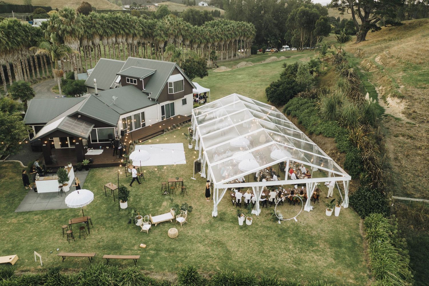 Aerial view of an outdoor wedding venue with a clear tent and farmhouse on a scenic hillside property.