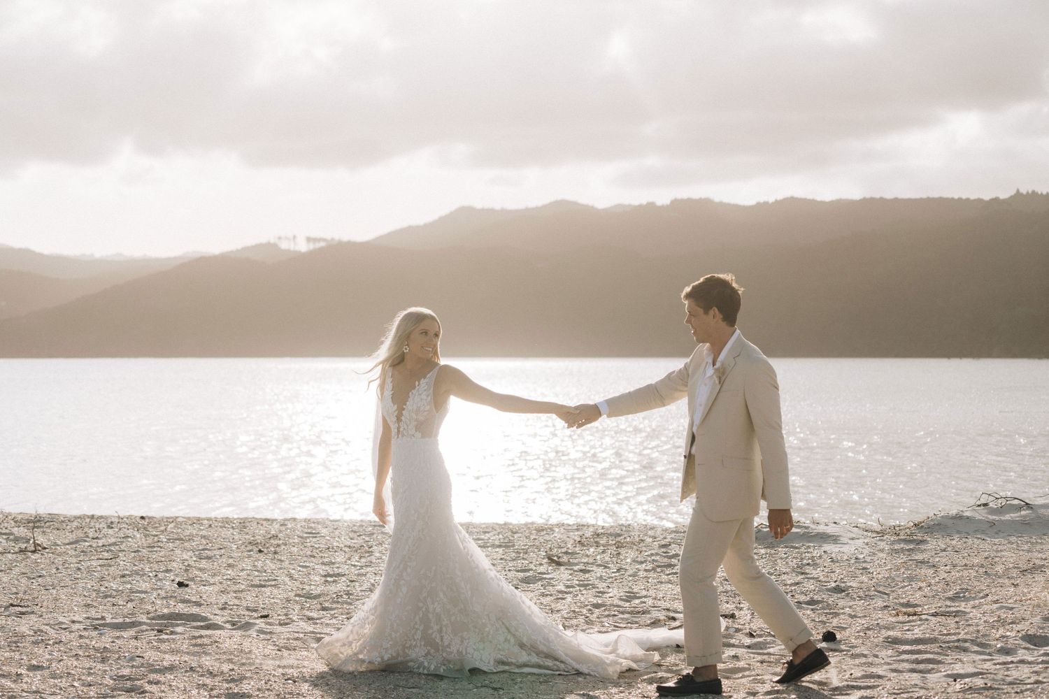Romantic sunset silhouettes on beach with mountains and water in background.