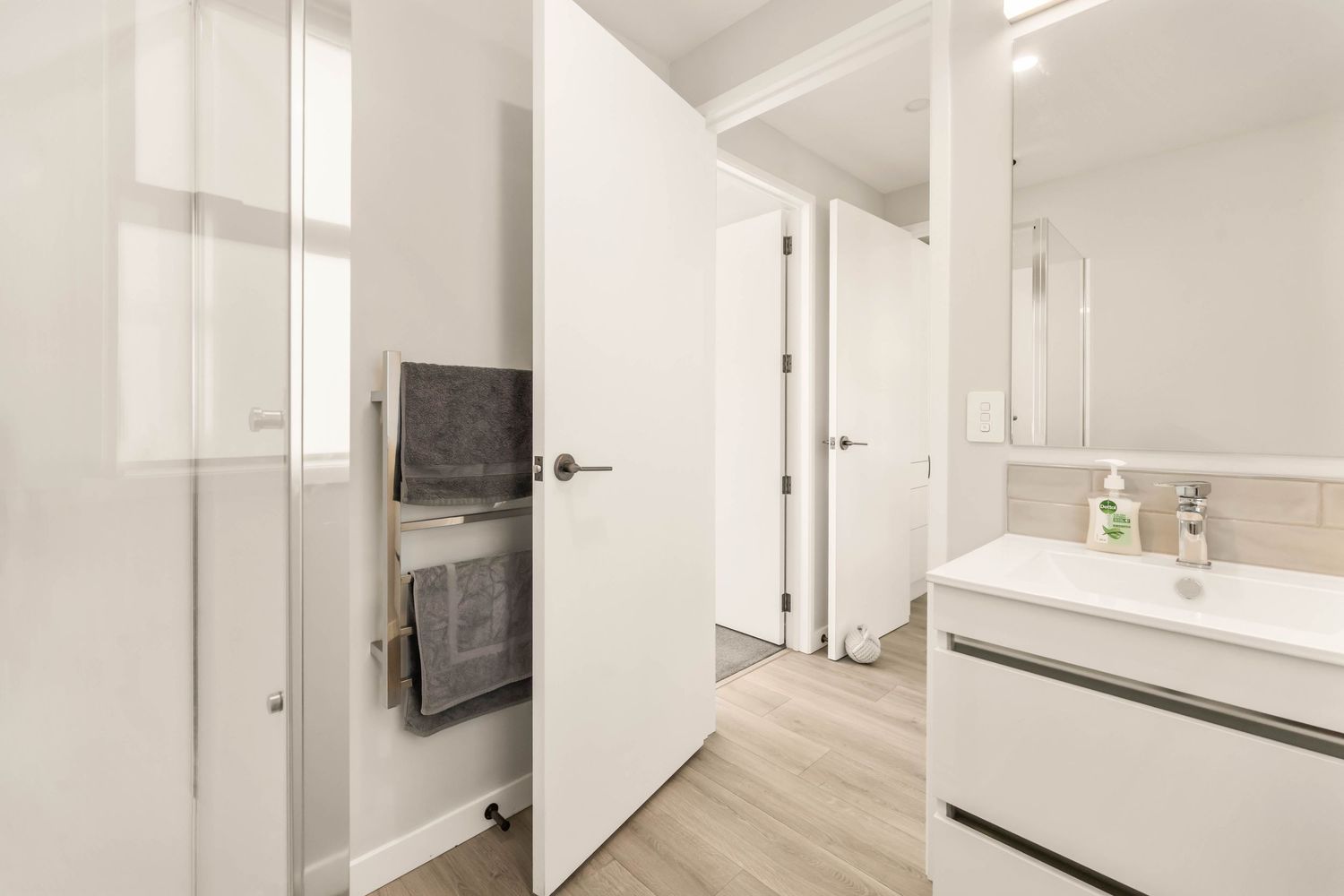 White modern bathroom with floating vanity, heated towel rack, and wood-look flooring.