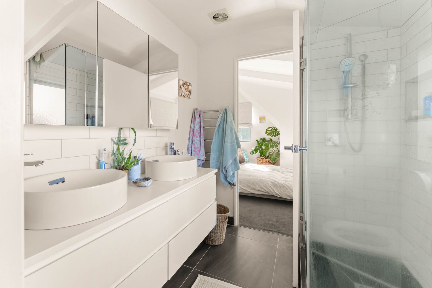 Modern white bathroom interior with floating vanity, glass shower enclosure and dark floor tiles.