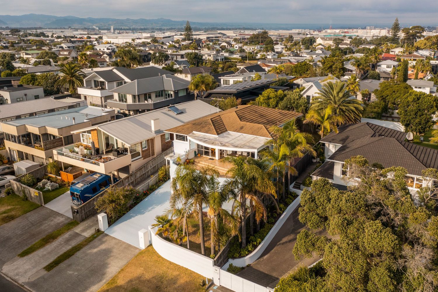 Aerial view of residential neighborhood in coastal area with palm trees and suburban homes under cloudy sky.