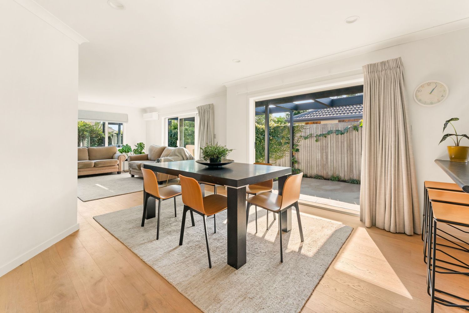 Spacious dining room with black table, orange chairs and floor-to-ceiling windows overlooking garden.