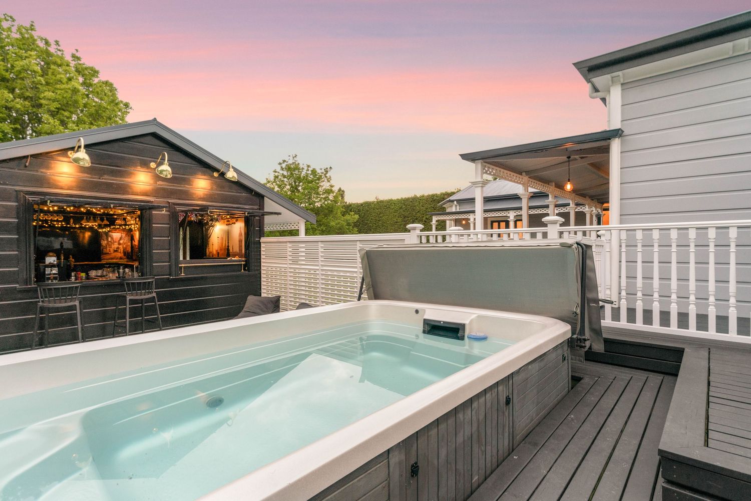 Hot tub on wooden deck with black shed and pink sunset sky in background.