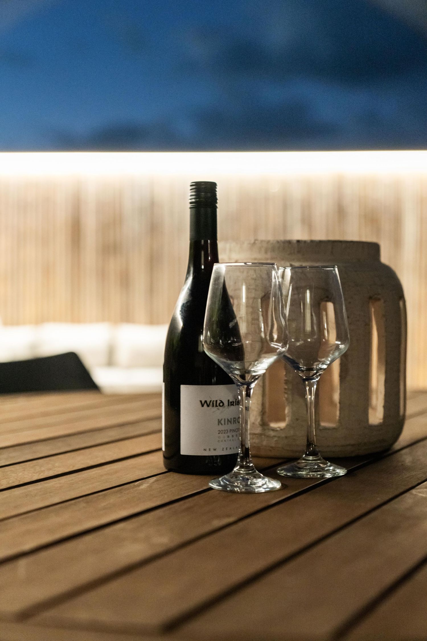 Wine glasses and bottles casting long shadows on wooden table in evening light.