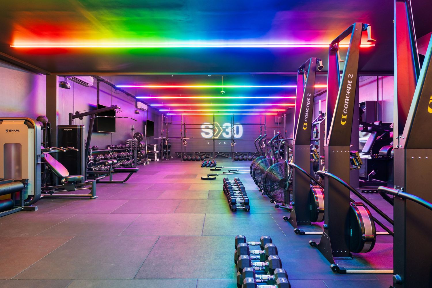 Spacious fitness facility with workout equipment arranged under colorful rainbow LED ceiling lights.
