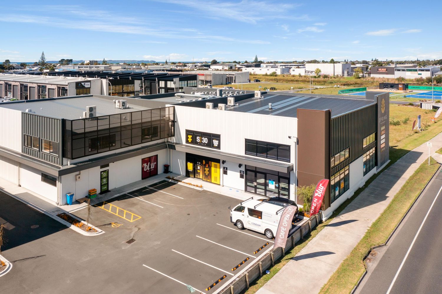 Modern commercial warehouse building complex with white walls and black trim features loading docks and parking lot.