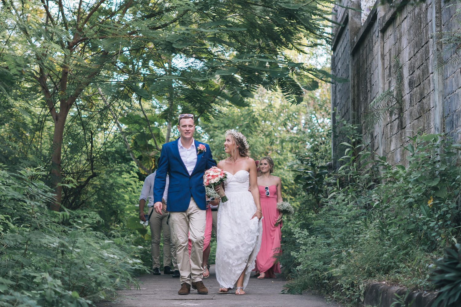 Three people walking along a lush garden path surrounded by greenery.