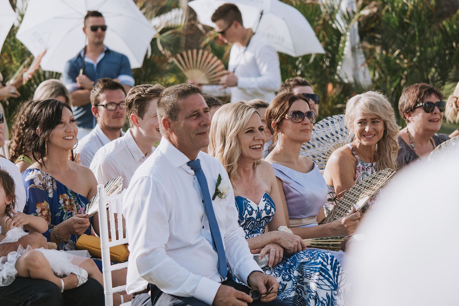 Wedding guests seated in white chairs watch the ceremony with smiles and joy.