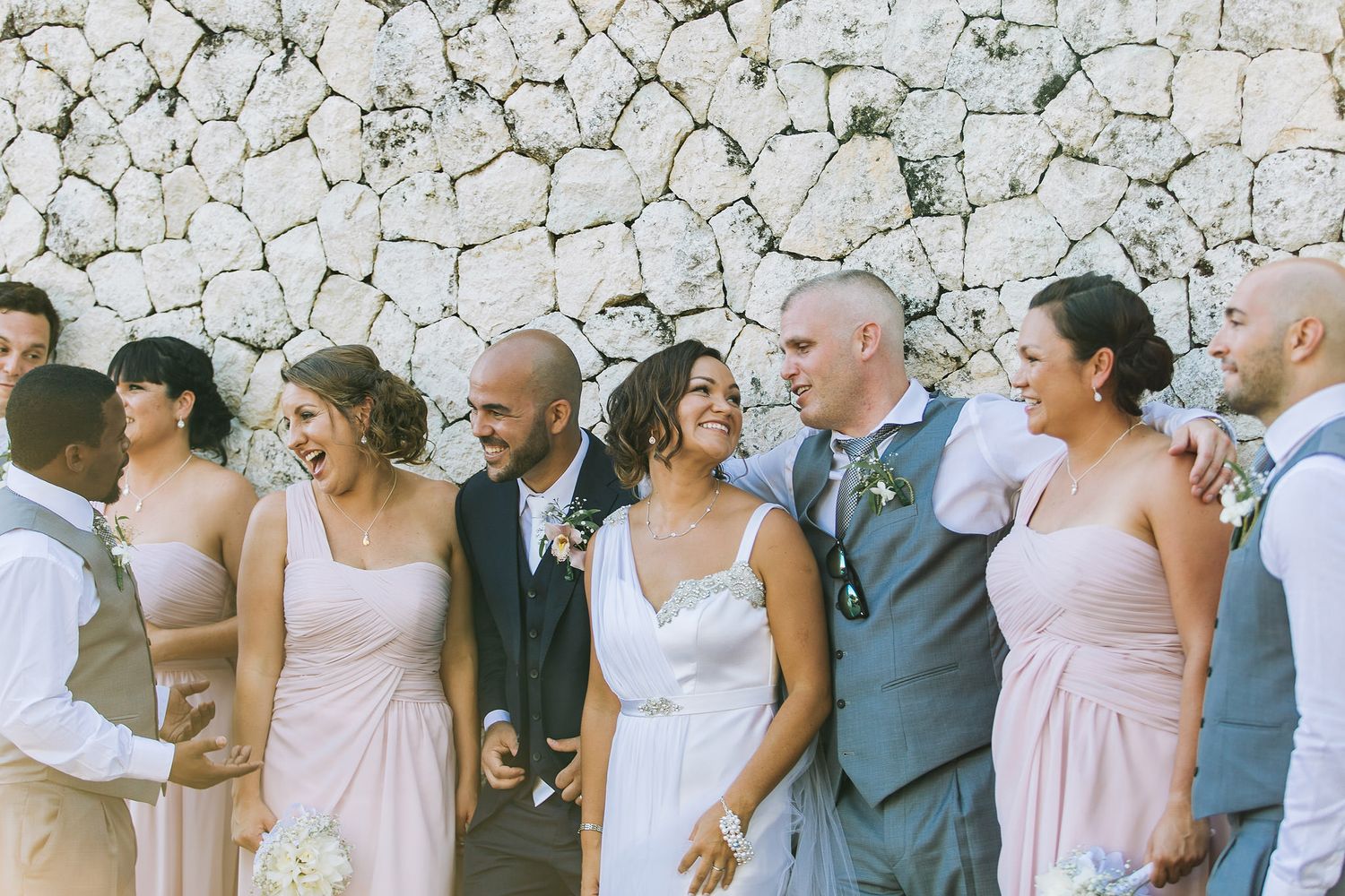 Wedding party lined up against a stone wall wearing pink and gray attire.