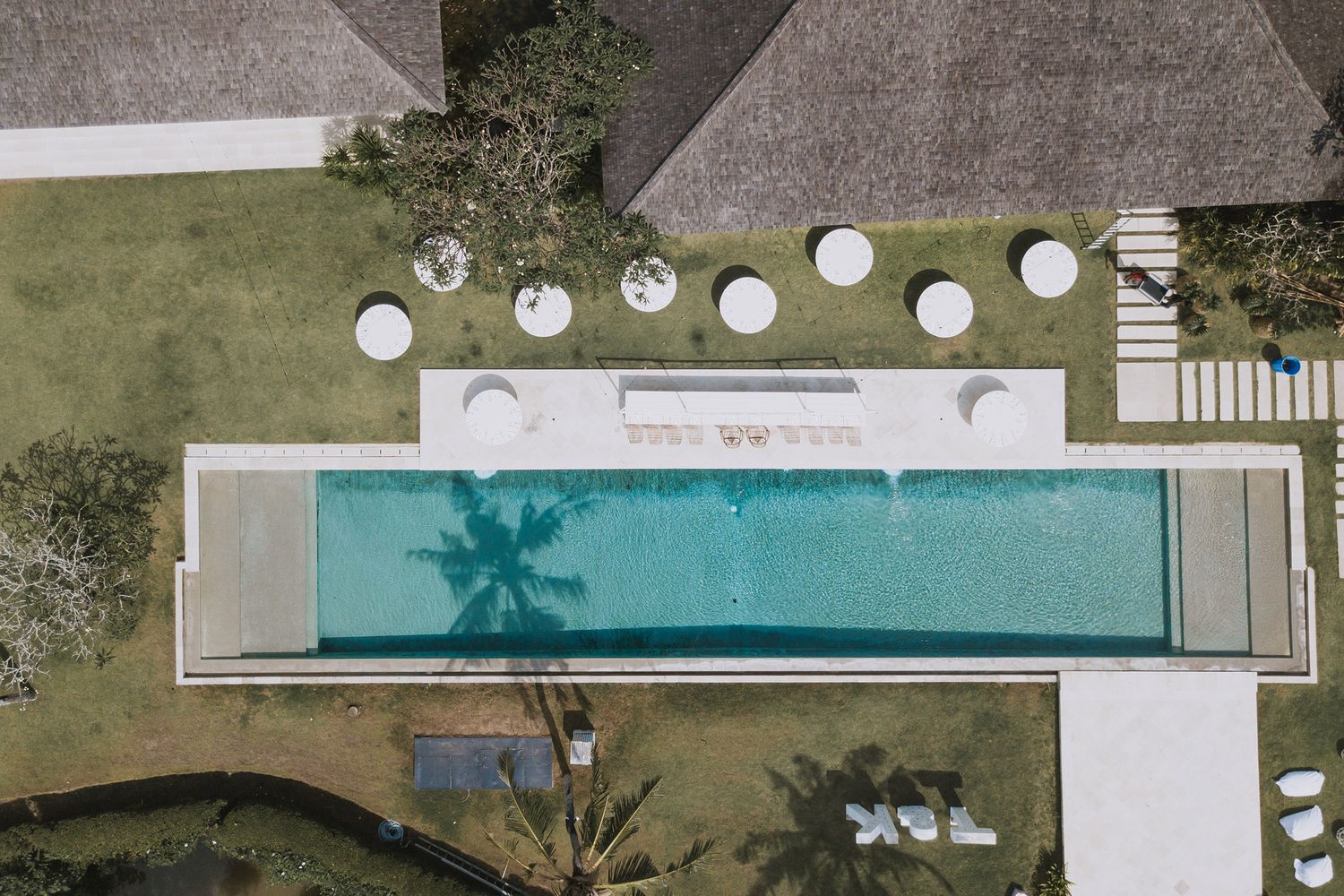 Aerial view of a luxury swimming pool with white sun loungers and thatched roof structures in a tropical setting.