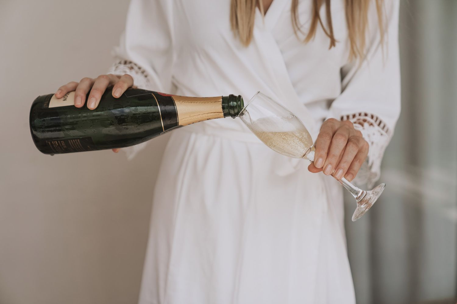 A person in a white dress pours champagne from multiple bottles into glasses on an elegant tabletop.