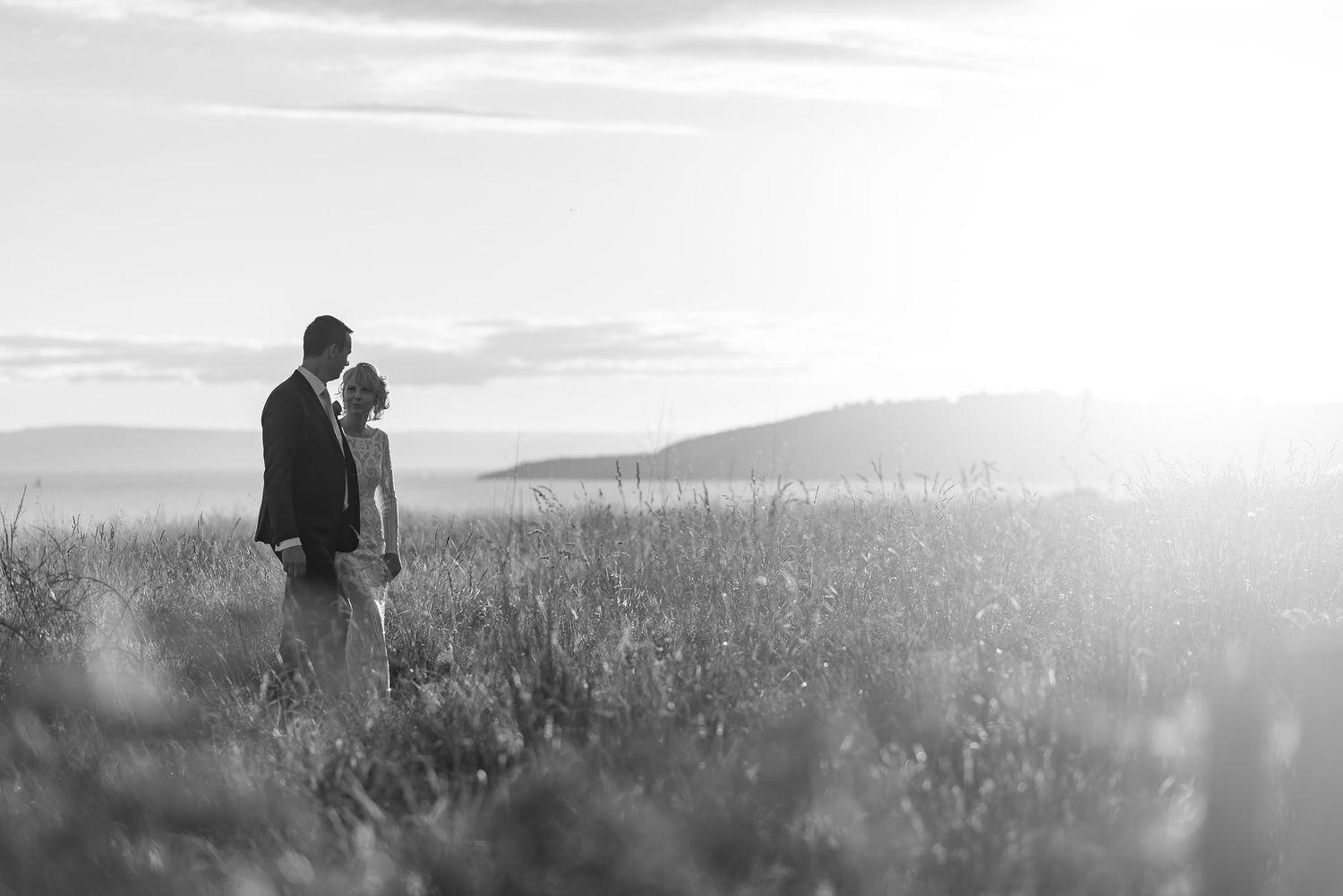A romantic silhouette of a couple standing in a misty meadow at sunset, captured in black and white.