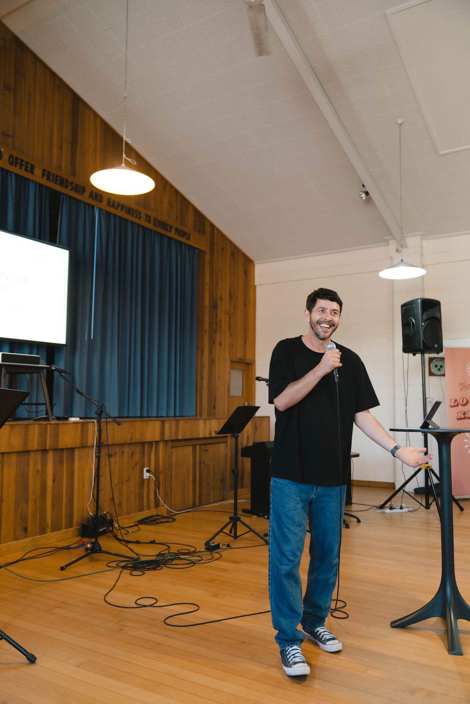 A speaker addresses the congregation from a wooden stage in a church hall.