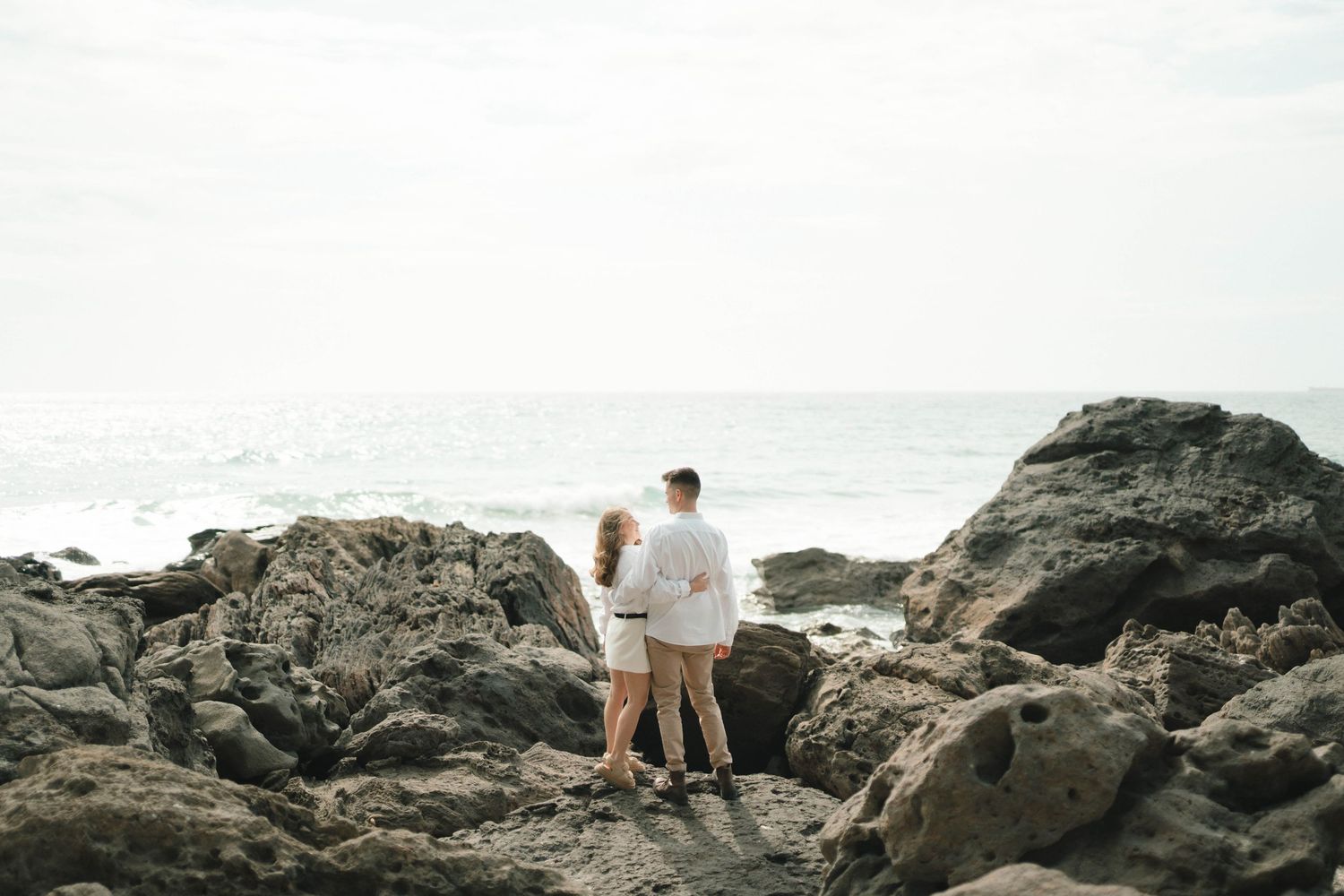 A romantic couple walks along scenic rocky seaside cliffs during sunset creating a silhouetted panoramic view.